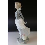 A Lladro figurine of a young woman with wind swept dress and basket of flowers at her feet.