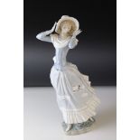 A Lladro figure of a woman holding her hat in a wind blown dress