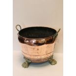 A twin handled antique copper log basket with strap work decoration raised on three paw feet.