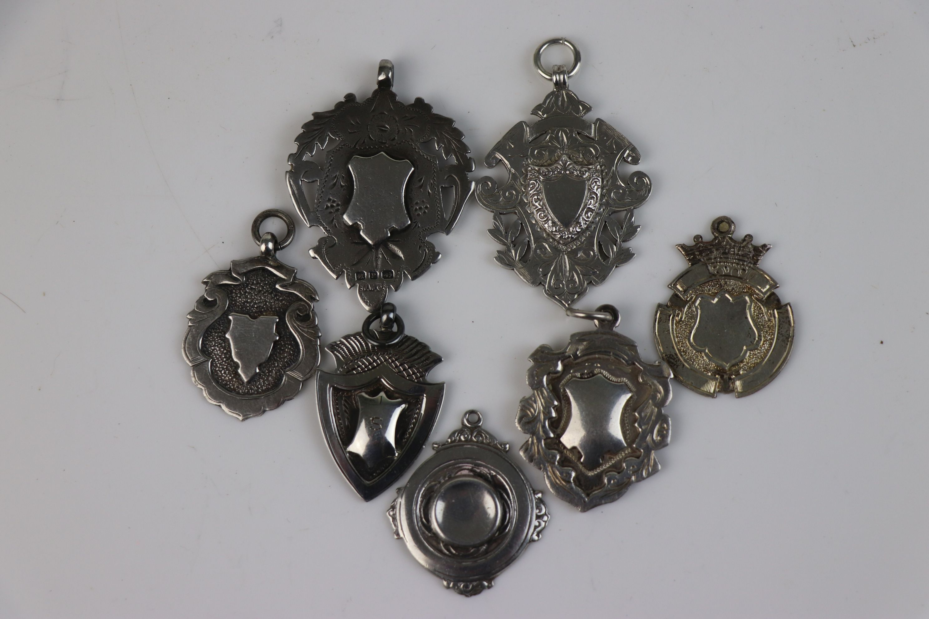 A collection of seven fully hallmarked sterling silver watch fob medallions.