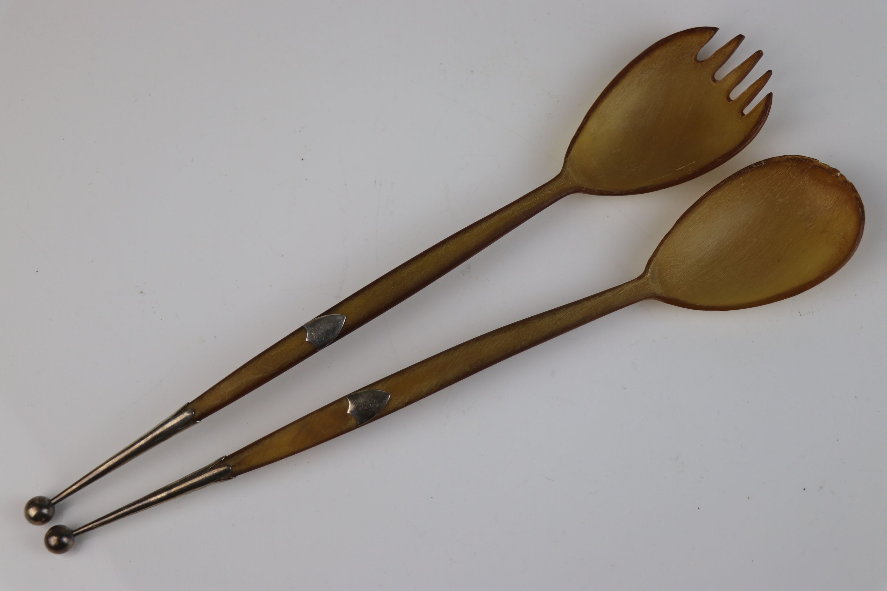 A pair of carved horn salad servers with sterling silver shield cartouche and finials, maker