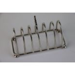 George V silver seven bar toast rack of arched form raised on four bun feet with trefoil finial,