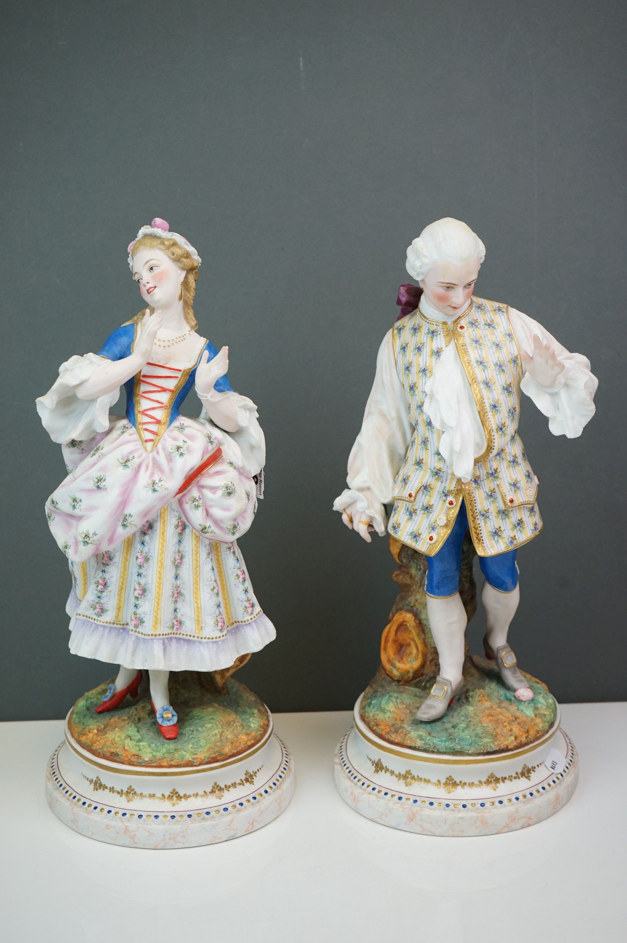 A pair of Continental bisque figures lady and gent in 18th century costume Makers mark AM 35 CM
