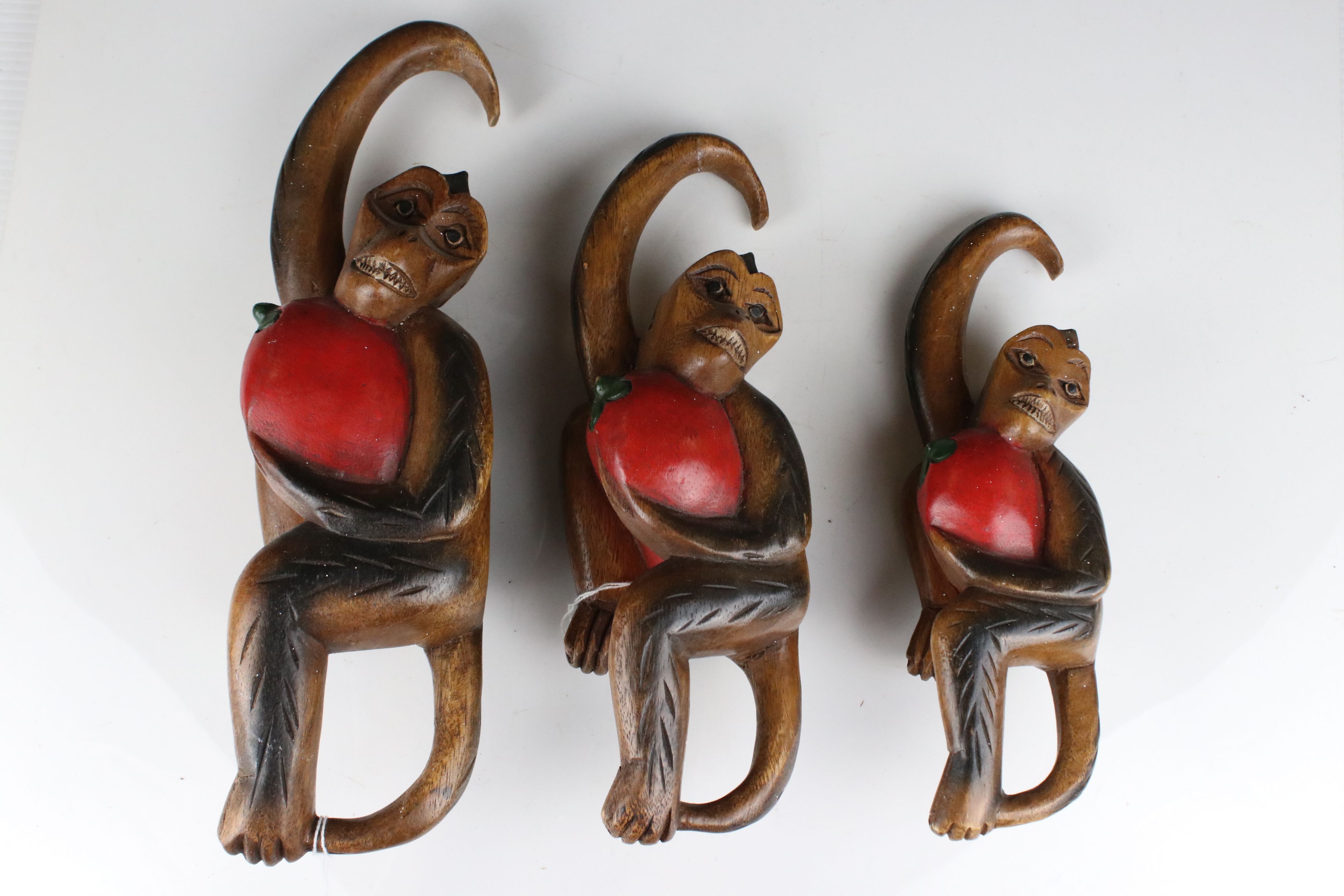 Three Carved Wooden Hanging Monkeys holding Fruit, largest 36cms high