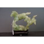 A carved jade figure of a horse with foal on wooden base.