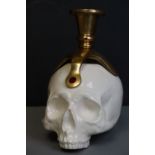 A white ceramic skull with mounted brass candle holder.