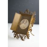 An ornate brass table top picture frame with folding doors with a picture of a Victorian lady.