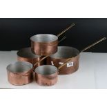 A set of five graduated copper saucepans with brass handles.