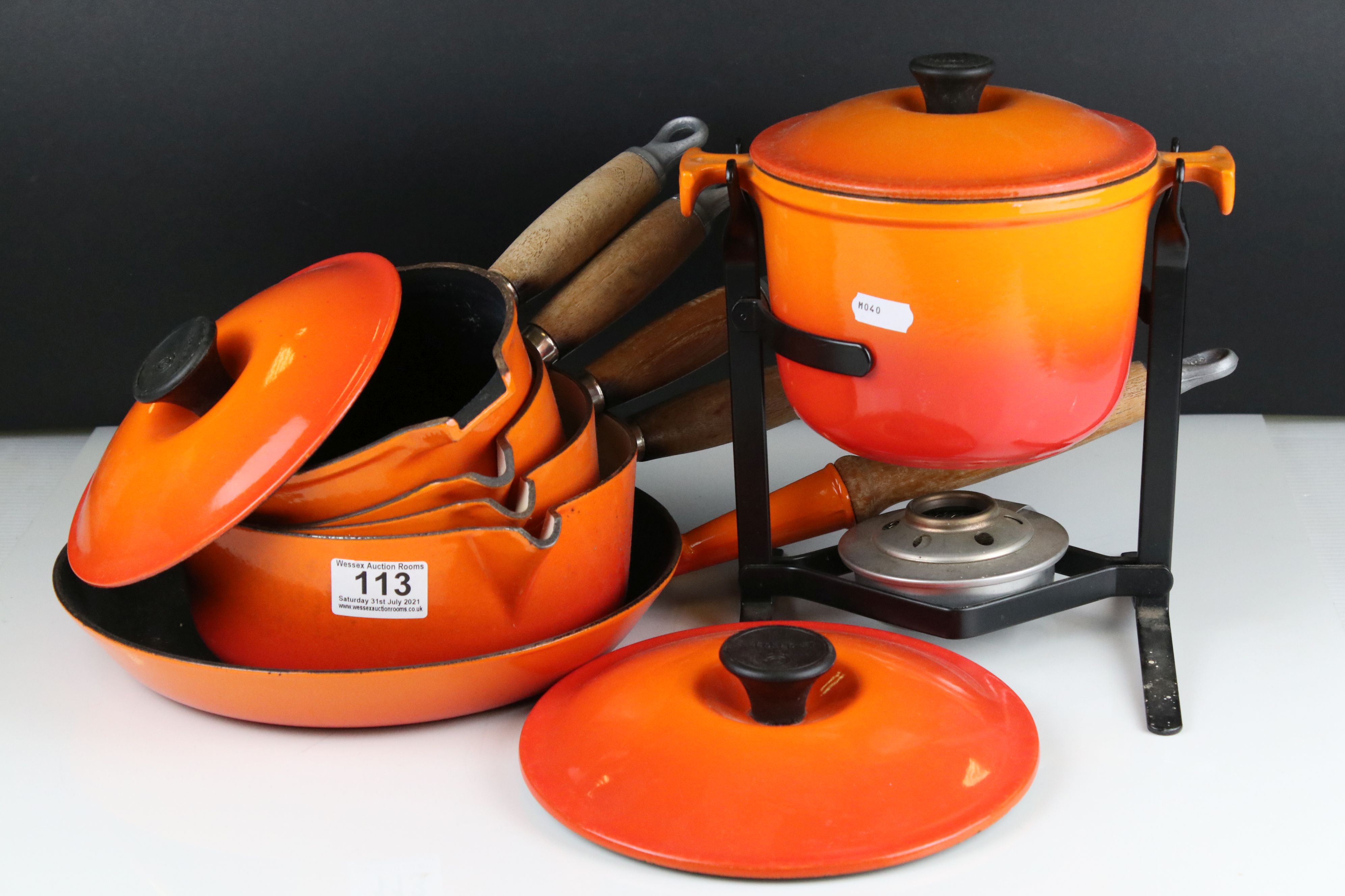 A collection of Le Creuset cast iron red pots and pans together with a fondue pan and burner.