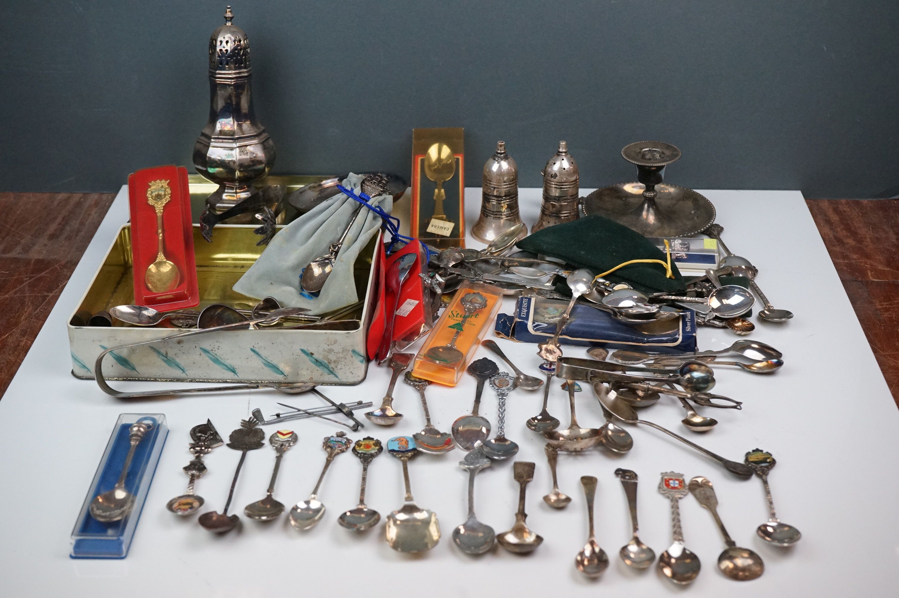 A mixed box of silver plated items to include collectors spoons, candle holder and sugar shaker.