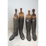 Two pairs of vintage black leather riding boots together with wooden boot trees.
