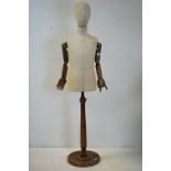 Child Shop Mannequin with articulated wooden arms, cloth body and raised on a turned wooden base,