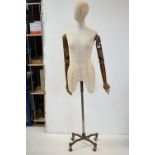 Female Shop Mannequin with articulated wooden arms, cloth body and raised on a metal industrial