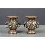 Two bronze miniature twin handled urns, with raised bird decoration to each panel, the handles