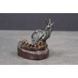A bronze figure of a snail aloft a skeletal jaw, signed.