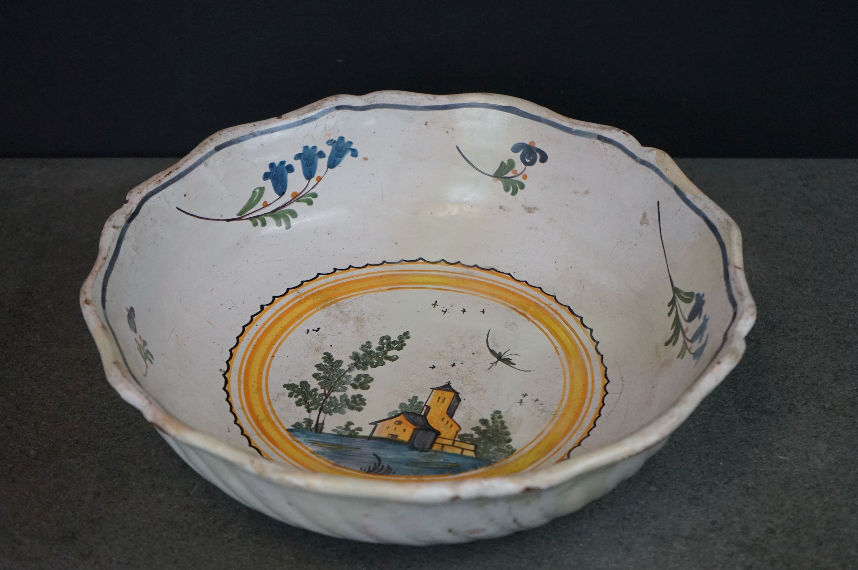 A vintage tin glaze bowl with central scene and floral surround.