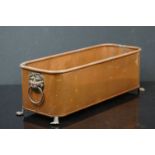 A copper rectangular planter with brass lion head handles.