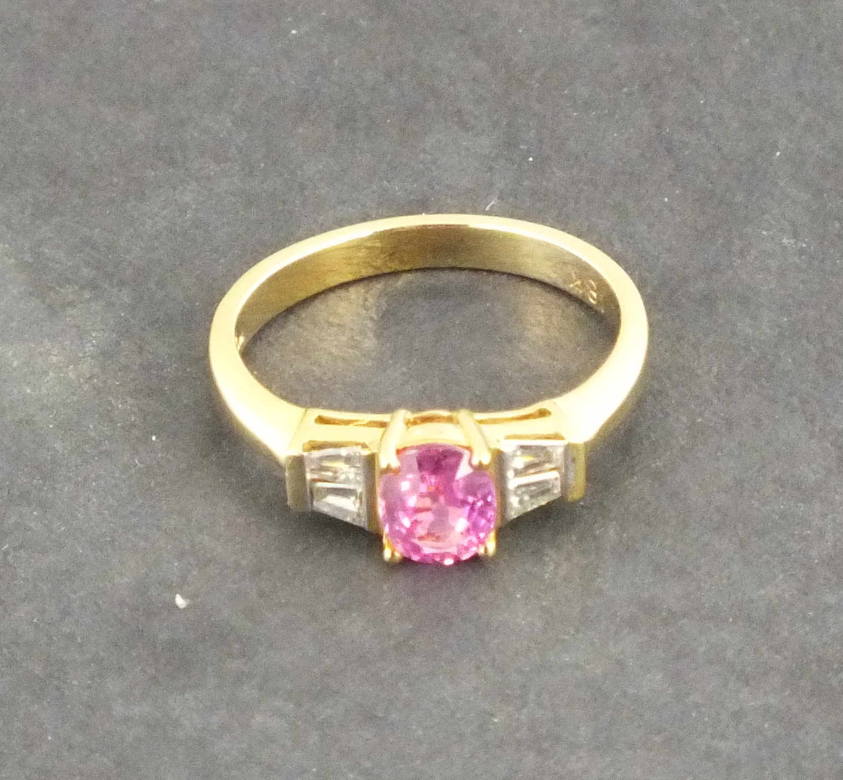 A pink sapphire and diamond dress ring, the central stone flanked by baguette cut diamonds, with a