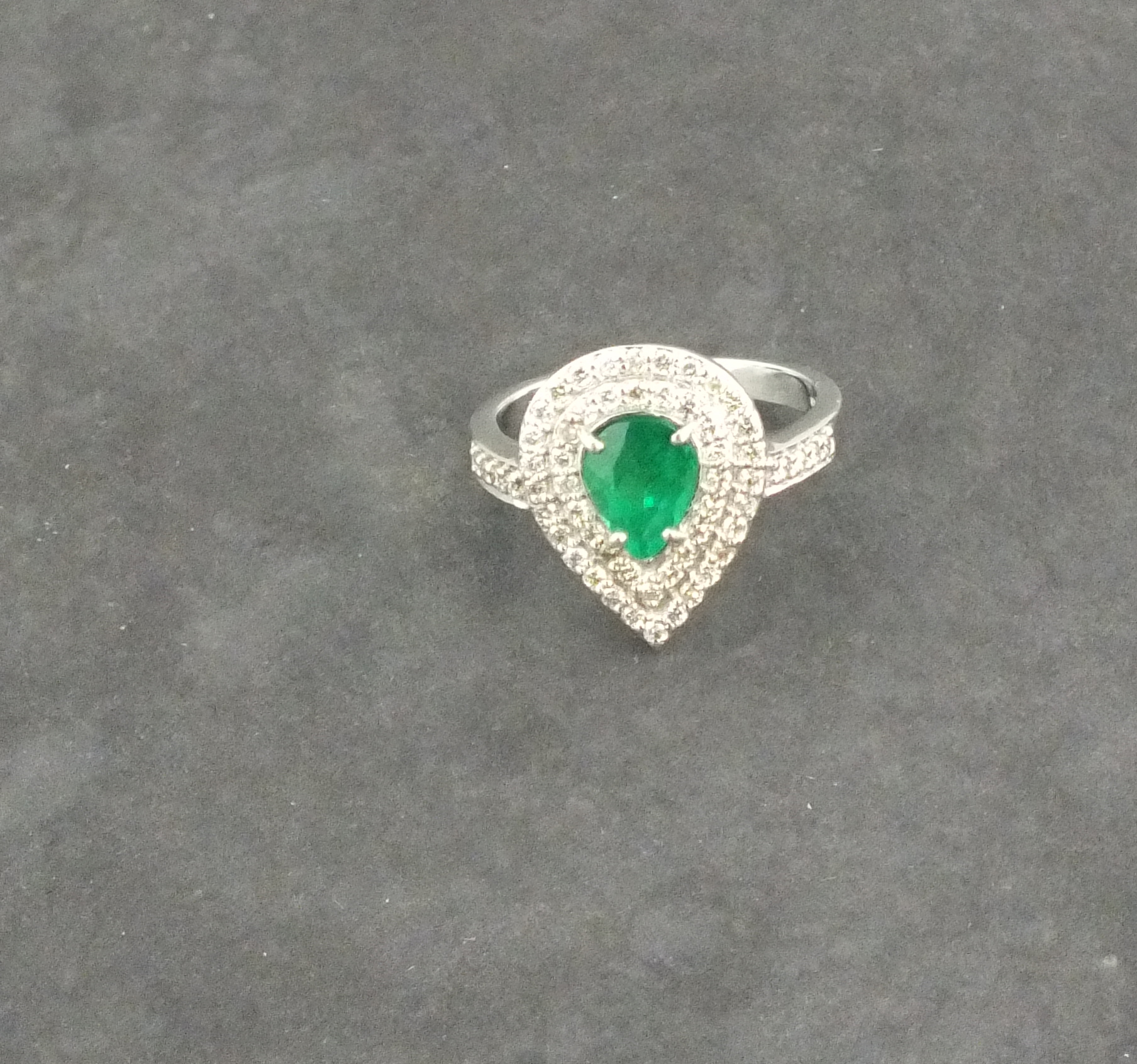 A emerald and diamond set dress ring, the pear shaped central stone set in 18ct white gold, 5.2gms