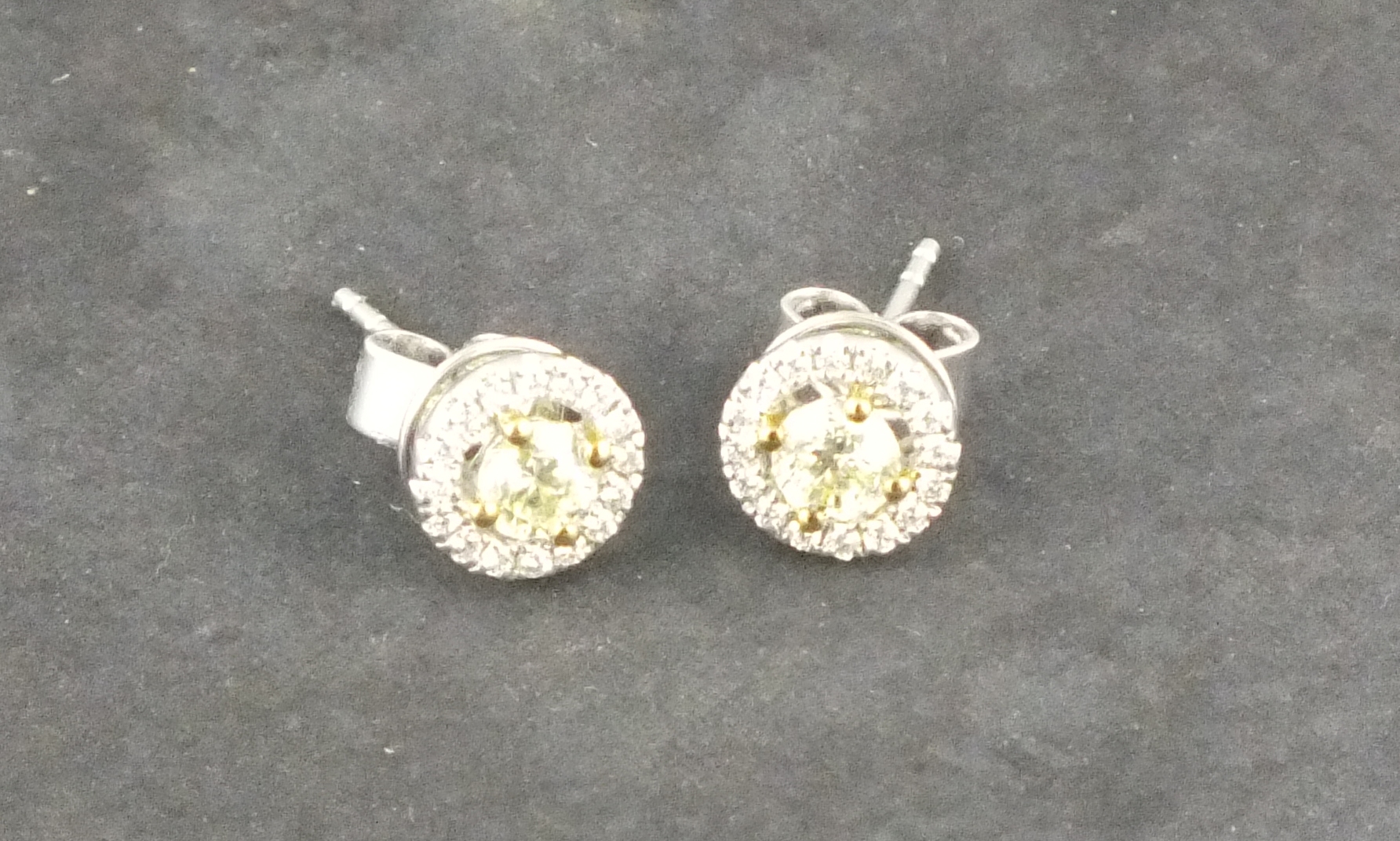 A pair of diamond ear studs, the fancy yellow brilliant cut stones within a halo of smaller stones