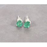 A pair of emerald ear studs, claw set in silver