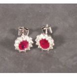 A pair of ruby and diamond studs, claw set in 18ct white gold, the oval cut central stones withing a