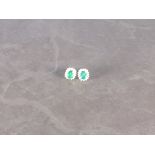 A pair of emerald and diamond ear studs, the central stones approx. 3.94ct, within a band of