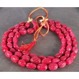 A string of red beads in three rows, oval and carved with a foliate design, on an adjustable cord