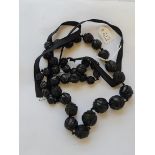 A row of graduated antique carved black jet beads with ribbon tie
