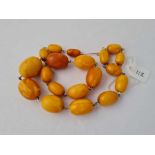 A GRADUATED OVAL AMBER BEADS STRUNG ON WIRE LARGEST BEAD 26 MM X 17.7 MM DIA 17 INCHES IN LENGTH -