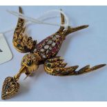 AN EARLY GEM ENCRUSTED FLYING BIRD BROOCH HOLDING A GEM ENCRUSTED HEART TO BEAK SET IN GOLD THE