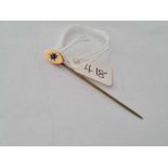 A oval topped stick pin with central sapphire set in gold