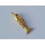 A gold charm in the form of a articulated fish with inset ruby eyes