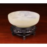 A Fine Pale Celedon Green Jade Bowl with raised foot, mounted on a carved & ebonised wooden stand.