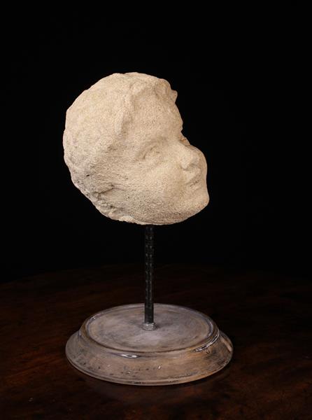 A Late 17th/Early 18th Century Carved Limestone Head of a Putto, mounted on a turned wooden base,