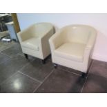 A pair of faux leather cream tub chairs, some usage marks but generally good