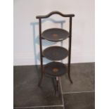 An Edwardian three tier cake stand with decorated shelves on four outswept legs, 74cm tall, in