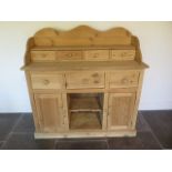 A stripped pine dresser with a four drawer shaped top over three drawer and two cupboard doors -