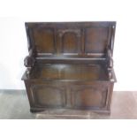 A darkwood carved and panelled monks bench with crouching lion arm rests and hinged seat with