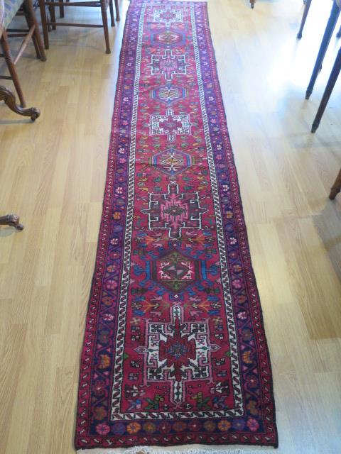 A hand knotted woollen runner with a red field, generally good condition, 340cm x 66cm