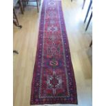 A hand knotted woollen runner with a red field, generally good condition, 340cm x 66cm