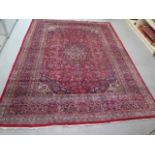 A large hand knotted woollen rug with a red field, 340cm x 245cm, some wear mainly to central part