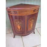 An Edwardian inlaid mahogany bow fronted corner cupboard with two urn inlaid doors on splayed