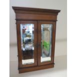 A satin walnut fronted small cabinet with two mirrored doors enclosing a mirror back shelved