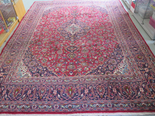 A hand woven large red ground Persian woollen Kashan carpet, 405cm x 284cm, some wear consistent