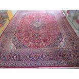 A hand woven large red ground Persian woollen Kashan carpet, 405cm x 284cm, some wear consistent