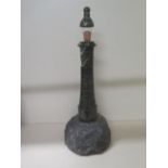 A Cornish serpentine lighthouse lamp with a glass shade on a rocky outcrop, 56cm tall x 20cm wide,