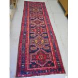 A blue and red ground hand woven runner with a cross door design, some wear but colours bright,