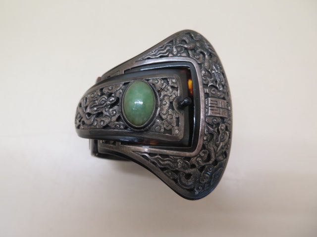 A Chinese folding tortoiseshell and white metal bangle set with a green jade cabouchon, 7cm wide