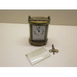 An oval brass carriage clock not currently running, front glass loose, 13cm tall with handle down